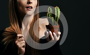 Frustrated woman with long silky straight hair in black body holding cactus plant in pot and comparing with split ends