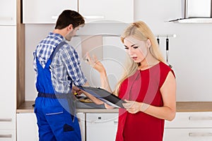 Frustrated Woman Looking At Bill On Clipboard In Kitchen