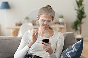 Frustrated woman looking at smartphone sitting on couch