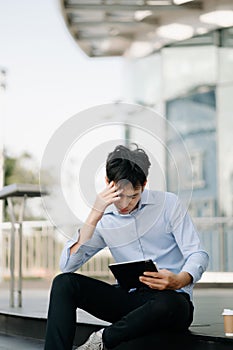 Frustrated young Asian businessman working on a laptop computer sitting at his working place in office