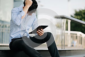 Frustrated young Asian businessman working on a laptop computer sitting at his working place in outside office