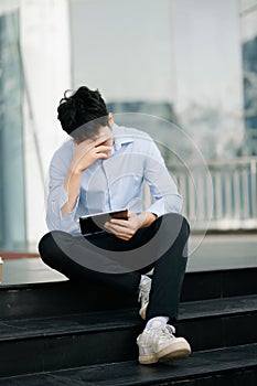 Frustrated young Asian businessman working on a laptop computer sitting at his working place in outside office