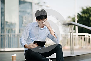 Frustrated young Asian businessman working on a laptop computer sitting at his working place in outside office