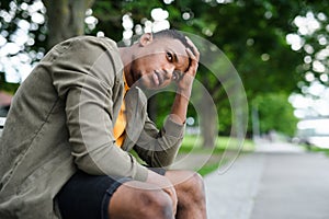 Frustrated young black man sitting on bench outdoors in city, black lives matter concept.