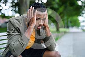 Frustrated young black man sitting on bench outdoors in city, black lives matter concept.