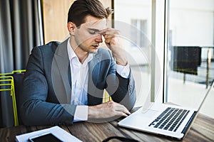 Frustrated young business man working on laptop computer at office
