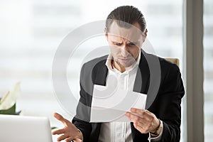 Frustrated young businessman looking at confusing letter in offi