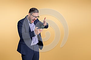 Frustrated young businessman looking and pointing at smart phone while screaming angrily. Male professional yelling aggressively
