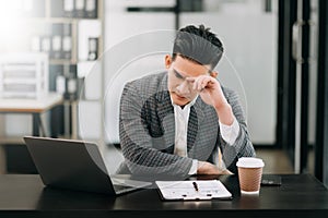 Frustrated young businessman working on a laptop computer sitting at his working place in modern office