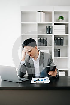 Frustrated young businessman working on a laptop computer sitting at his working place in office