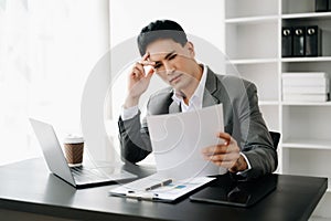 Frustrated young businessman working on a laptop computer sitting at his working place in office