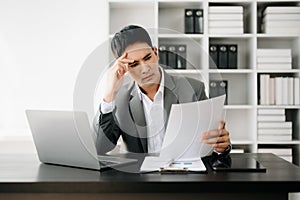 Frustrated young businessman working on a laptop computer sitting at his working place in office