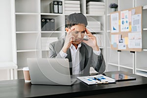 Frustrated young businessman working on a laptop computer sitting at his working place in office