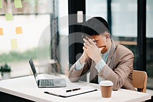 Frustrated young businessman working on a laptop computer sitting at his working place in office