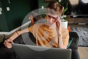 Frustrated young caucasian man in casual clothing by laptop on sofa in living room at home