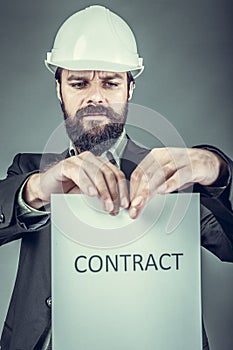 Frustrated young engineer with hardhat tearing apart a contract