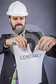 Frustrated young engineer with hardhat tearing apart a contract