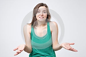 Frustrated young girl in green clothes shrugging shoulders