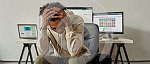 Frustrated young guy, trader holding head, feeling depressed about debt after stock market business failure, sitting at