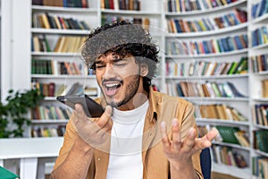 Frustrated young man with curly hair arguing on phone in library