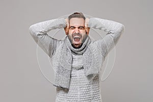 Frustrated young man in gray sweater, scarf posing isolated on grey background. Healthy fashion lifestyle, cold season