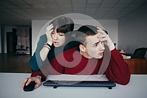 Frustrated young office workers near the computer. Emotional beautiful young people in the workplace.