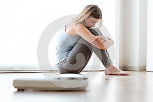 Frustrated young sad woman after seeing her weight on the scale at home.