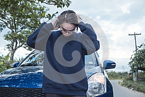A frustrated young woman in a blue sweater hopelessly breaks down outside when her car fails to start while on a road trip