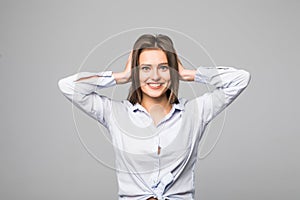 Frustrated young woman covering ears by hands and keeping eyes closed while standing against grey background