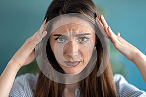 Frustrated young woman with headache and frowning while looking at camera at home