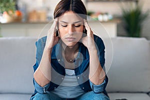 Frustrated young woman with headache and frowning while sitting on couch in the living room at home