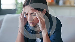 Frustrated young woman with headache and frowning while sitting on couch in the living room at home