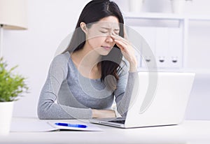 Frustrated young woman keeping eyes closed and massaging nose while sitting at home office