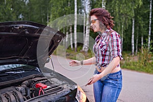 Frustrated young woman looking at broken down car engine