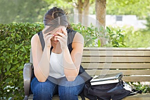 Frustrated Young Woman Sitting Alone on Bench Next to Books