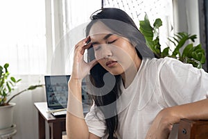 Frustrated young woman working at desk in front of laptop suffering from daily chronic headaches, online treatment