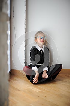 Frustration state of mind crying upset little caucasian girl in glasses and school uniform sitting on floor near window