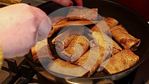 Fry wrapped pancakes in pan closeup. Female hands flip stuffed pancakes with wooden spatula. Russian cuisine, food.