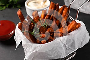 Frying basket with sweet potato fries and sauces on black table, closeup