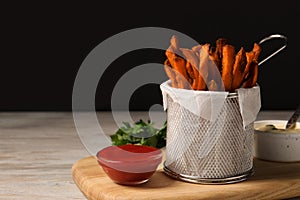 Frying basket with sweet potato fries, sauces and parsley on table. Space for text