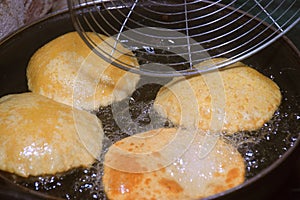 frying chapati(poori) with spoon on frying pan, boiling oil in frying pan with dark background, kitchen concept