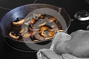 Frying chestnut mushrooms, with a man holding a cast iron frying pan with a tea towel, on an electric hob