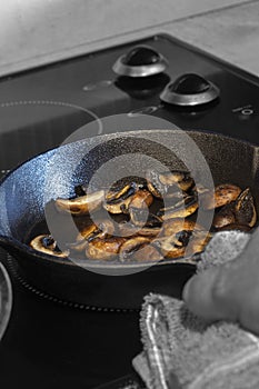 Frying chestnut mushrooms, with a man holding a cast iron frying pan with a tea towel, on an electric hob