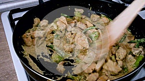 Frying chicken with broccoli on a black pan. Mixing cream in with wooden spatula. Cooking dinner at home on a week night.