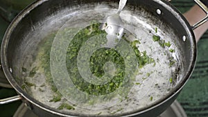 Frying chopped fresh dill plants inside old pan on oven