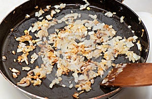 Frying chopped onion with vegetable oil in a frying pan. Stirring the onion with a wooden spatula
