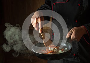 Frying onions with carrots in a pan in the hands of a cook. Space for a recipe or menu on a dark background. European cuisine