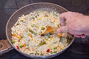 Frying pan closeup of cooking rice with vegetables and herbs. Wooden kitchen spatula for mixing ingredients while preparing