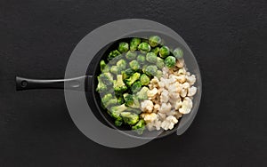 Frying pan with frozen vegetables on a black background. Cauliflower, broccoli, Brussels sprouts. Cabbage mix. Top view, flat lay
