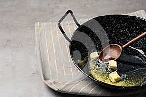 Frying pan with melting butter and wooden spoon on grey table